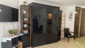 Een moderne woonkamer met een schuifdeurkast, een flatscreen televisie aan de wand en een zwarte leren fauteuil.
