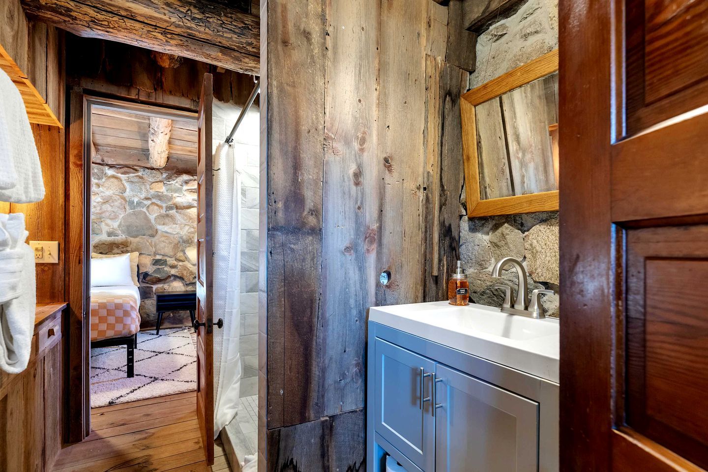 Ein rustikales Badezimmer mit Steinwand, Holztür und Waschbecken mit Spiegel darüber.