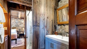 Ein rustikales Badezimmer mit Steinwand, Holztür und Waschbecken mit Spiegel darüber.