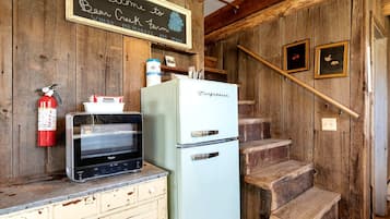 A rustic kitchen with a vintage refrigerator, a microwave, and a fire extinguisher.
