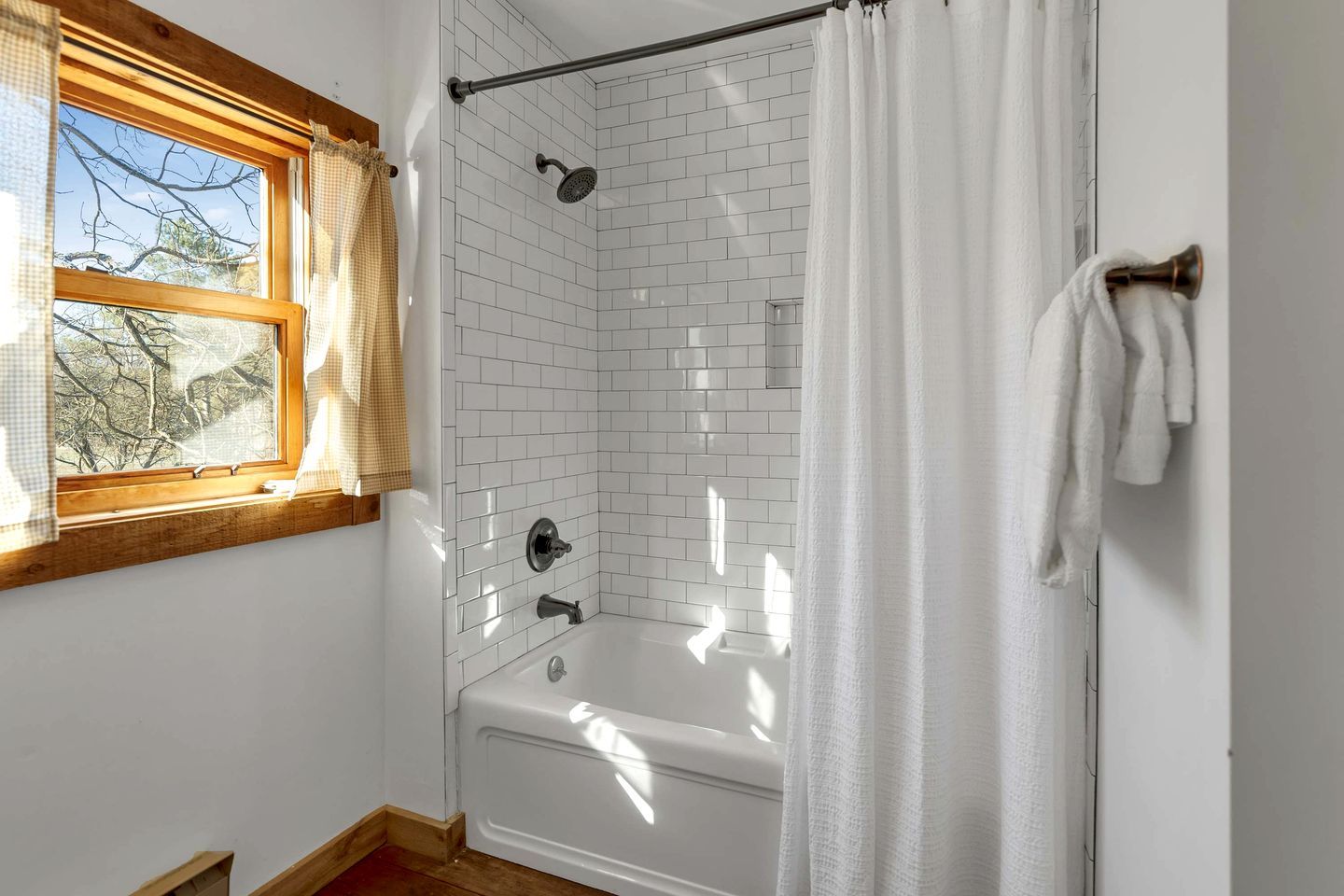 A bathroom with a bathtub, a shower, a window with curtains, and a towel rack.
