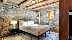 Ein Schlafzimmer mit Steinwänden, einem Bett, Nachttischen und einem mit Vorhängen drapierten Fenster.