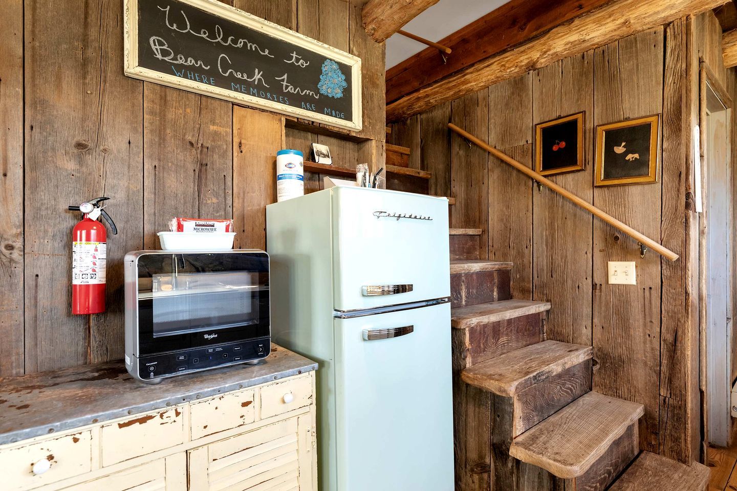 A rustic kitchen with a vintage refrigerator, a microwave, and a fire extinguisher.