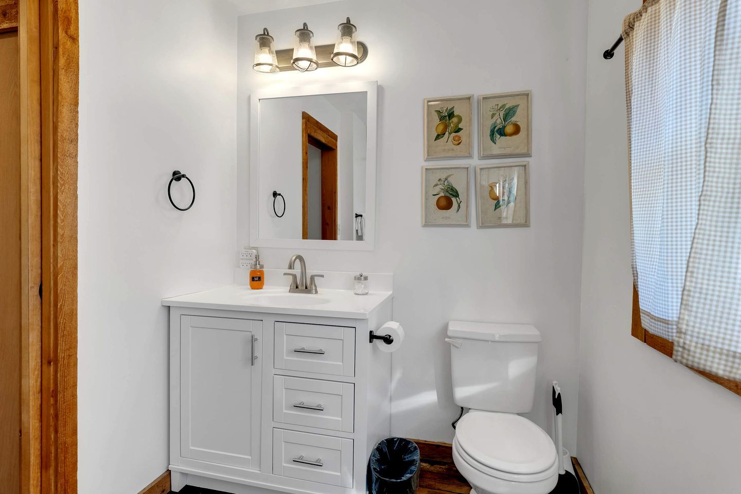 A bathroom with a white sink, mirror, and toilet. There are framed pictures on the wall and a towel hanging on the right.