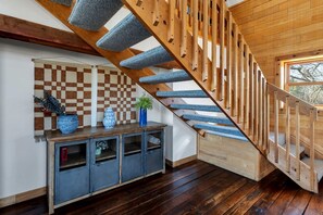 A wooden staircase with blue carpeted steps, a checkered wall, and a wooden console table with decorative items.
