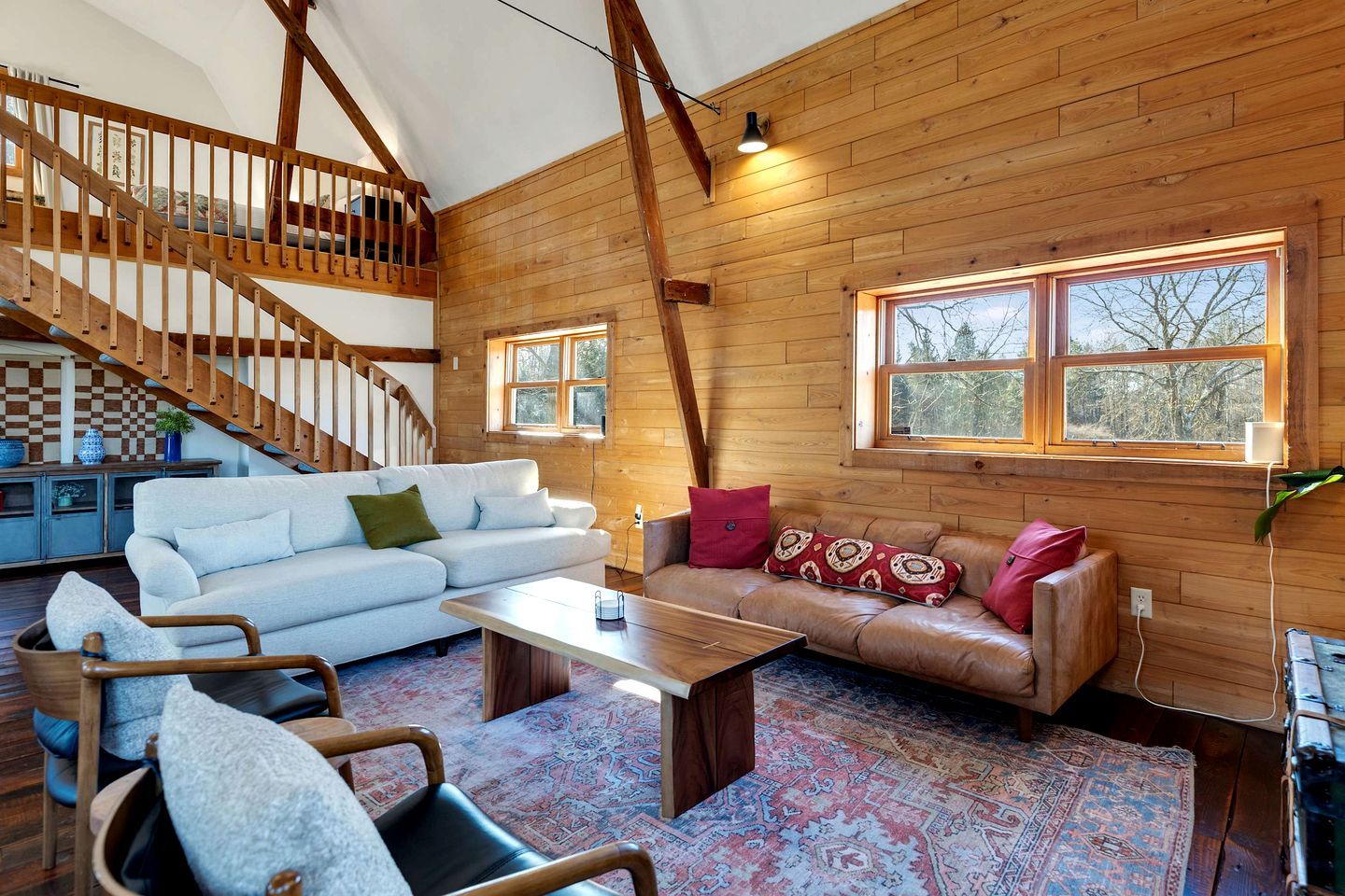 Un vaste espace de vie de style loft, doté d’un plafond haut, de poutres en bois, d’un escalier et de grandes fenêtres.