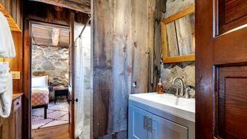 Une salle de bain rustique avec un mur en pierre, une porte en bois et un lavabo surmonté d’un miroir.