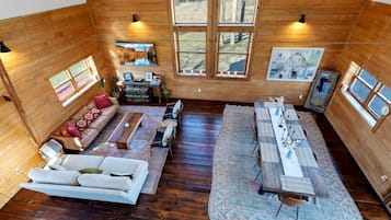 Amplia habitación con piso de madera, sofá, mesa de comedor con sillas y ventanas grandes con vista al exterior.