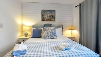 A hotel room with a checkered bedspread, two bedside lamps, a painting above the bed, and a curtain on the window.