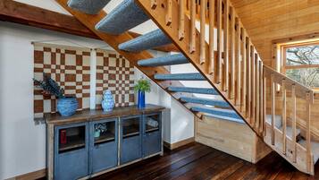 A wooden staircase with blue carpeted steps, a checkered wall, and a wooden console table with decorative items.
