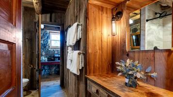 A wooden bathroom with a stone wall, a wooden door, a mirror, and a vase with flowers.