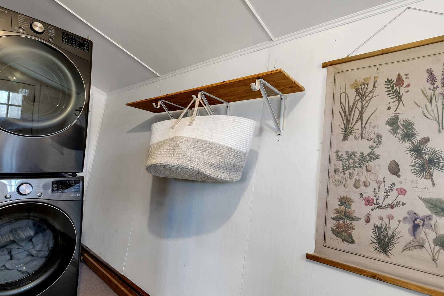 A laundry room with a washing machine, a dryer, and a hanging basket on a wooden shelf.