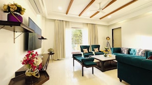 A modern living room with a TV, two green sofas, a coffee table, and a floor lamp. - Spark Banquet Hall South Delhi (New Delhi)