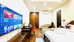 Habitación de hotel con televisión mostrando una selección de películas, un escritorio con una computadora portátil, una cama con colcha estampada y un armario.