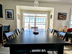 Un espace repas comprenant une longue table, des chaises et une vue dégagée sur l’extérieur grâce à une grande fenêtre.