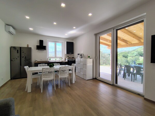 A modern kitchen with a dining area, wooden flooring, and a large sliding glass door leading to an outdoor patio.