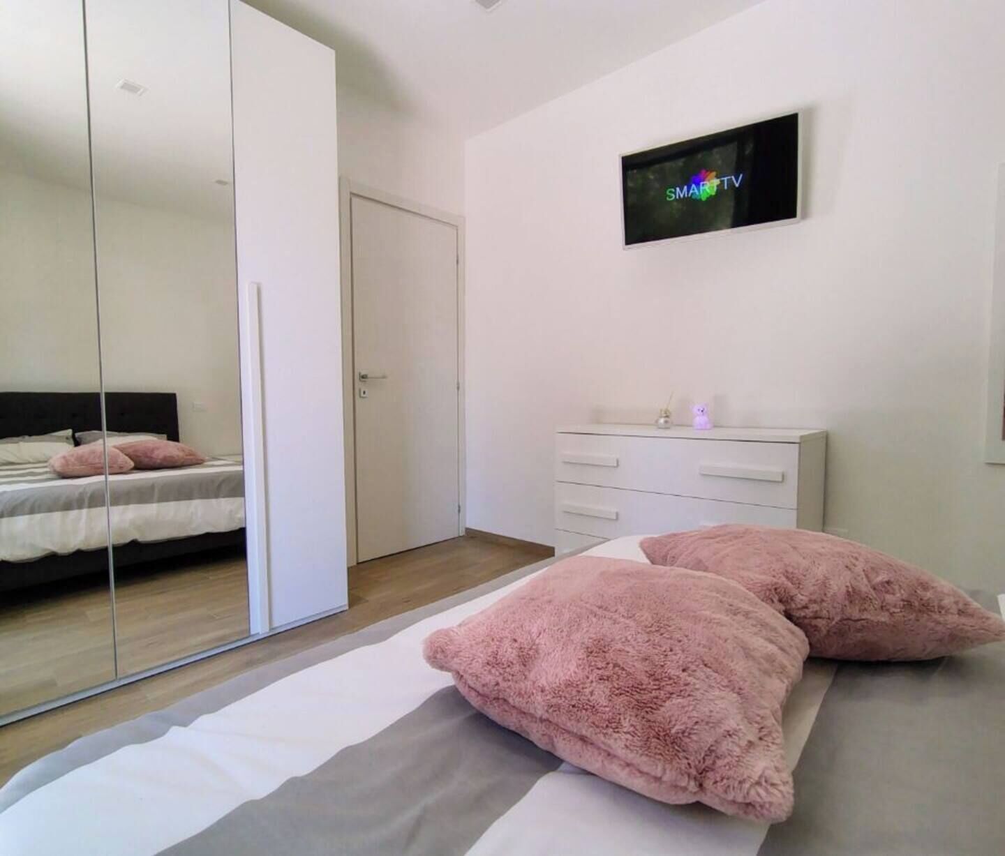 A bedroom with a bed, a dresser, a TV on the wall, and a mirrored closet door.