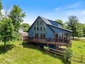 Une maison bleue avec une terrasse, entourée d’arbres et d’herbe.