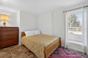 A bedroom with a bed, a dresser, a lamp, and a window with blinds. - Bright Mountain Cabin with Game Room & Golf Course Views Near Hedgesville, West Virginia (Hedgesville)