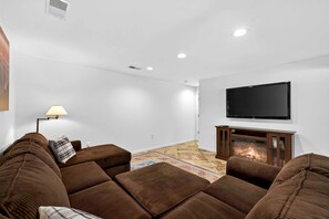 A modern living room with a flat-screen TV, a fireplace, and a sofa set. - Bright Mountain Cabin with Game Room & Golf Course Views Near Hedgesville, West Virginia (Hedgesville)