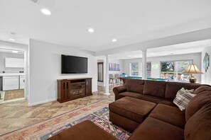 A living room with a brown sectional sofa, a flat-screen TV mounted on the wall, a wooden entertainment center, and a patterned rug. - Bright Mountain Cabin with Game Room & Golf Course Views Near Hedgesville, West Virginia (Hedgesville)