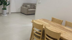 A modern interior with a dining area featuring a wooden table and chairs, a staircase with a railing, and a living space with a sofa and a potted plant.