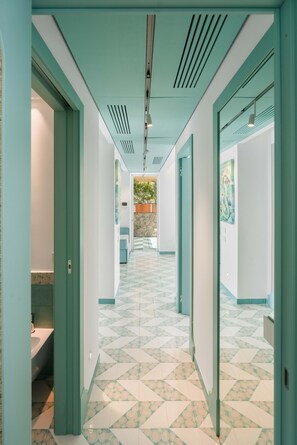 A hallway with geometric patterned flooring, green walls, and a visible bathroom with a sink and toilet. - Estate4home - Villa Nerea (Massa Lubrense)