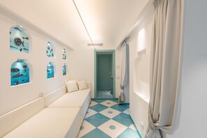 A narrow hallway with a bench, a teal and white tiled floor, and wall-mounted artwork. - Estate4home - Villa Nerea (Massa Lubrense)