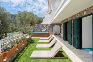 A poolside area with lounge chairs, a stone wall, and a view of the mountains. - Estate4home - Villa Nerea (Massa Lubrense)