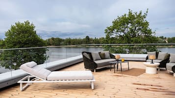 A deck with outdoor furniture, a glass railing, and a view of a lake.