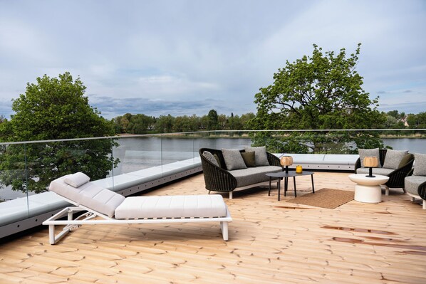 A deck with outdoor furniture, a glass railing, and a view of a lake.
