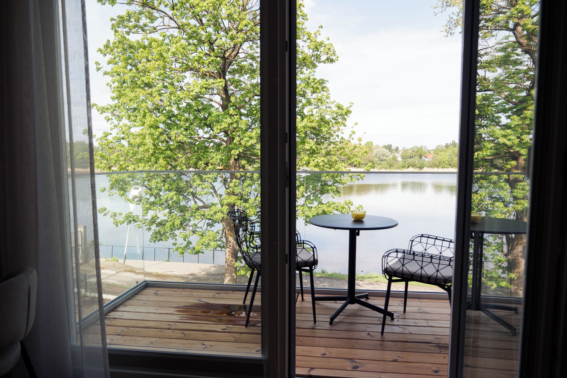 Una terraza de madera con una mesa y sillas, con vista a un lago rodeado de árboles.