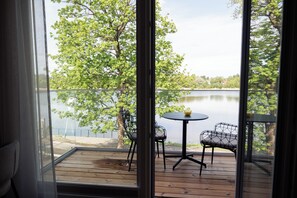 A wooden deck with a table and chairs, overlooking a lake with trees.