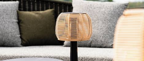 A wicker lamp on a small table, a sofa with cushions, and a wooden floor.
