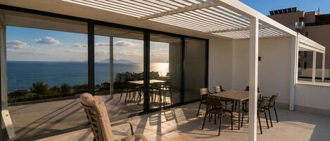 Un patio moderno al aire libre con zona de comedor, una mecedora y vista al mar.