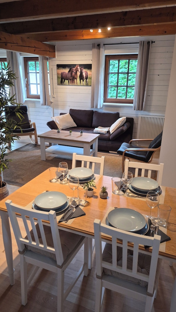 A dining area with a wooden table set for four, white chairs, and a sofa in the background.