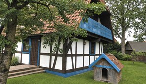 Une maison traditionnelle à colombages, dotée d’un balcon bleu et d’une petite niche en bois pour chien portant l’inscription « BALDU ».