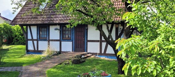 Une maison traditionnelle à colombages, dotée d’un toit en pente, d’une porte d’entrée et d’un petit jardin avec un chemin menant à l’entrée.
