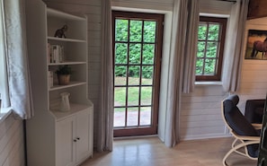 Ein Zimmer mit Holzboden, einem weißen Schrank mit Regalen, einem Fenster mit Vorhängen und einem Sessel.