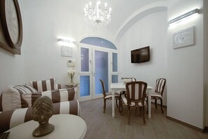 A living room with a sofa, chairs, a dining table, a chandelier, and a TV mounted on the wall. - Colosseo & Fori Imperiali Apartment (Rome)