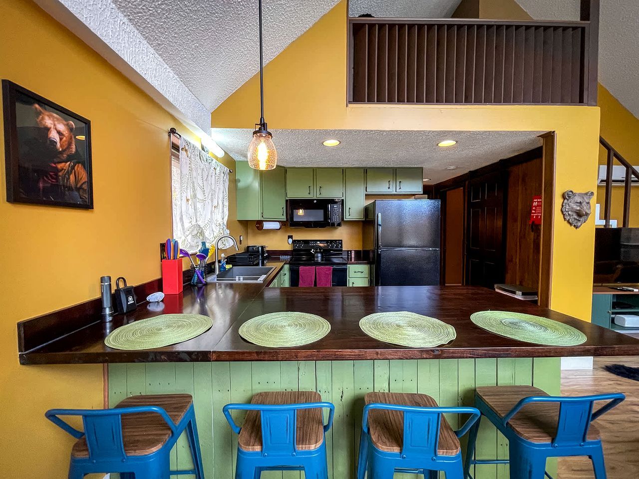 A kitchen with a central island, green cabinets, a microwave, and a refrigerator.