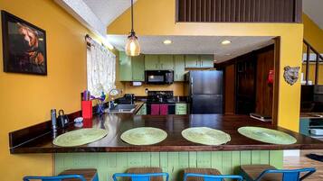 A kitchen with a central island, green cabinets, a microwave, and a refrigerator.