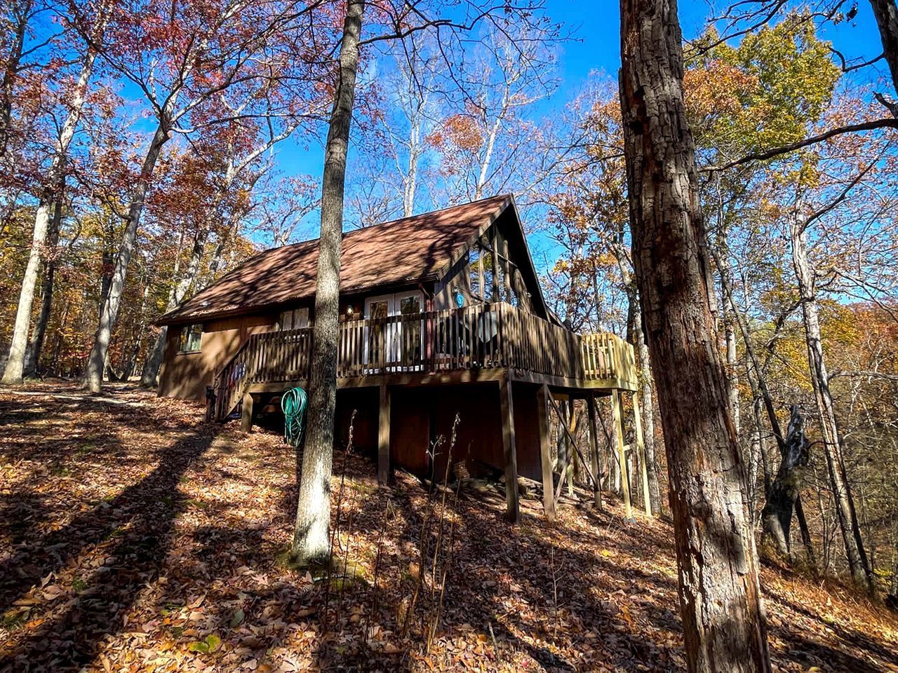 Un chalet rustique doté d’une terrasse en bois, entouré d’arbres et offrant une vue sur un ciel dégagé.