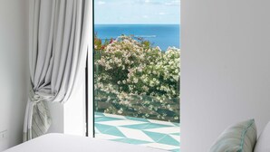 Un dormitori amb una finestra gran, un llit i vista al mar i flors.