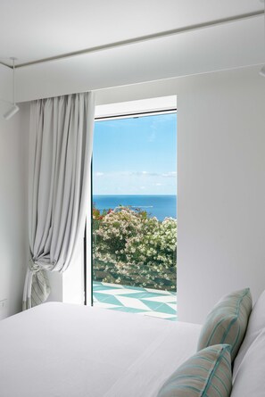 A bedroom with a large window, a bed, and a view of the sea and flowers. - Villa Nerea (Nerano)