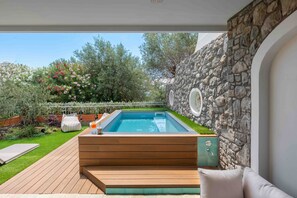 A swimming pool with a wooden deck and seating area, surrounded by a stone wall and lush greenery. - Villa Nerea (Nerano)
