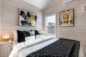 A bedroom with a bed, a nightstand, a window with blinds, and two wall-mounted artworks. - Luxury Hill Country Tiny Home in Resort Setting Near Fredericksburg, Texas (Fredericksburg)
