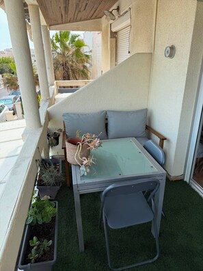 A balcony with a glass table, two grey chairs, a grey sofa, and potted plants. - 🌊 Two-bedroom apartment 30 m from the beach | Partial ocean view | Sleeps 4 | Carnon-Plage (Mauguio)