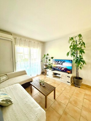 A living room with a sofa, a coffee table, a TV, and potted plants. - 🌊 Two-bedroom apartment 30 m from the beach | Partial ocean view | Sleeps 4 | Carnon-Plage (Mauguio)