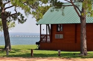 A wooden cabin with a green roof, a porch, and a grill outside. - Serene Lakeview Cabin in Buchanan Dam with Firepit & Outdoor Relaxation in Buchanan Dam, Texas (Buchanan Dam)